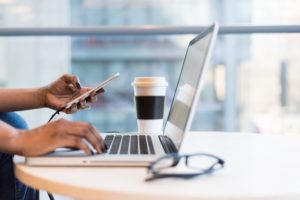 Woman holding a cell phone, while working at a laptop computer.